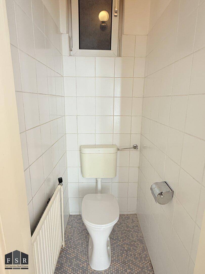 Kleines WC mit weiß gefliesten Wänden, Fenster und einem Heizkörper, in gutem Zustand und funktional.