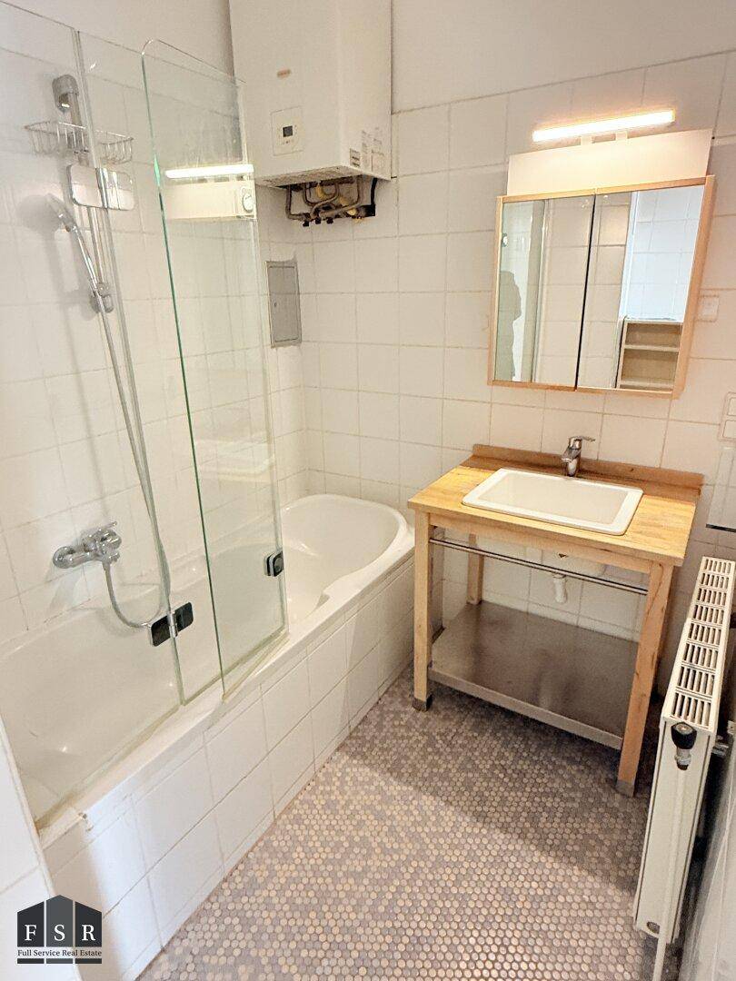 Badezimmer mit Badewanne, Duschabtrennung, Waschbecken und Spiegelschrank, weiß gefliest und funktional eingerichtet.