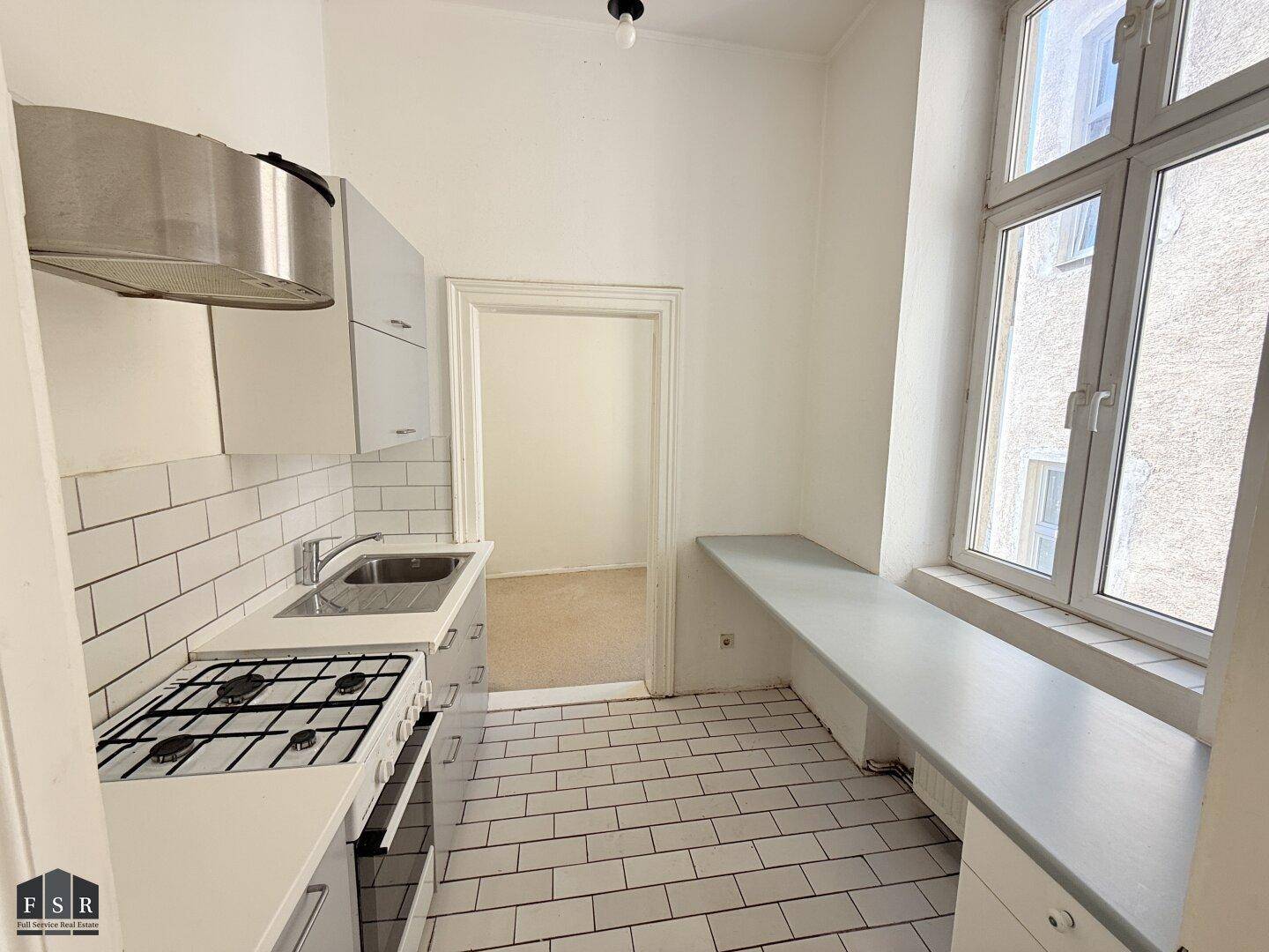 Kleine Küche mit Gasherd, Spüle, Dunstabzugshaube und einem Fenster mit Ablagefläche, praktisch gestaltet.