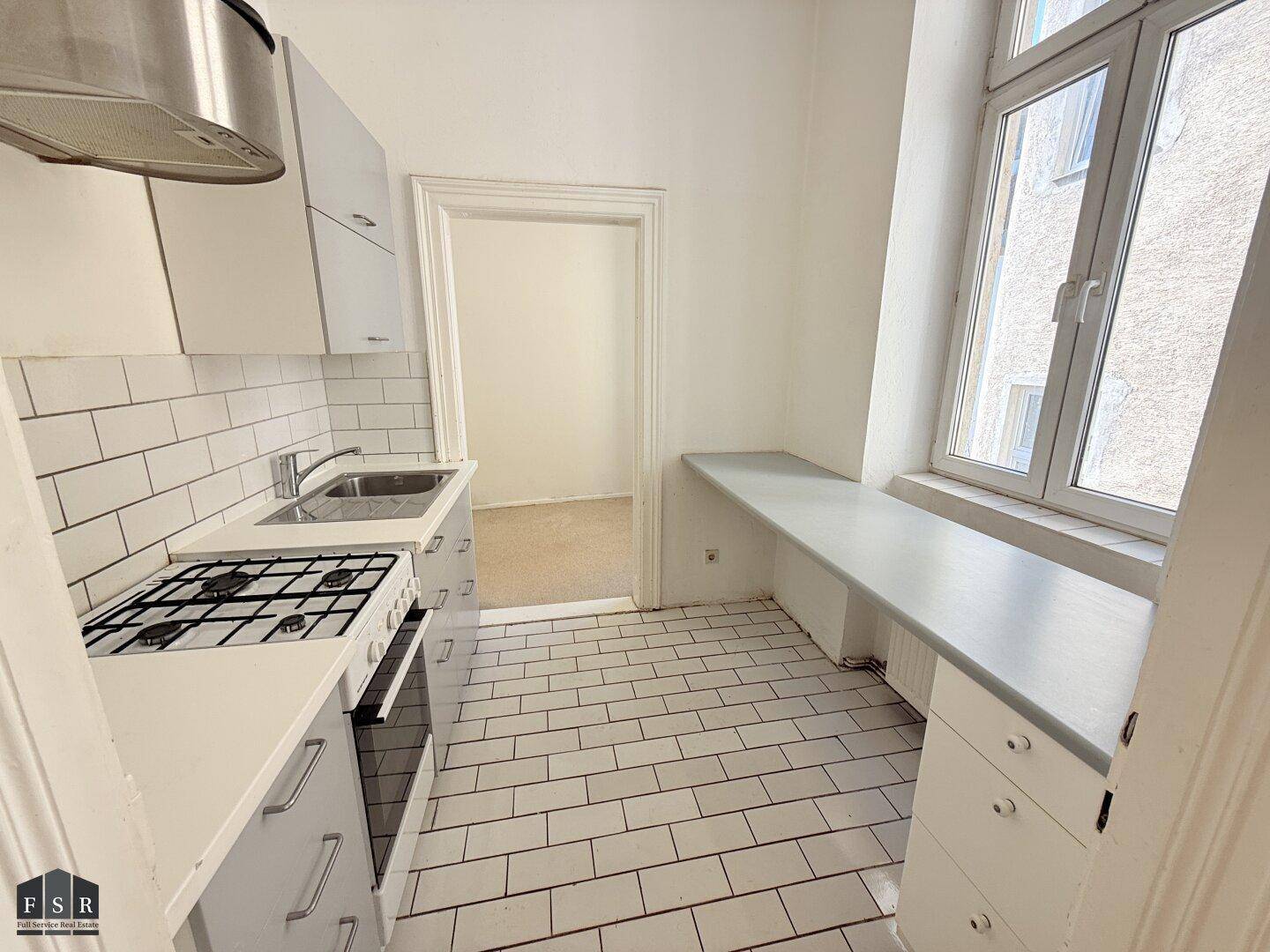Funktionale Küche mit weißen Fliesen, Gasherd und Fensterbank, bereit zur Nutzung und in gutem Zustand.