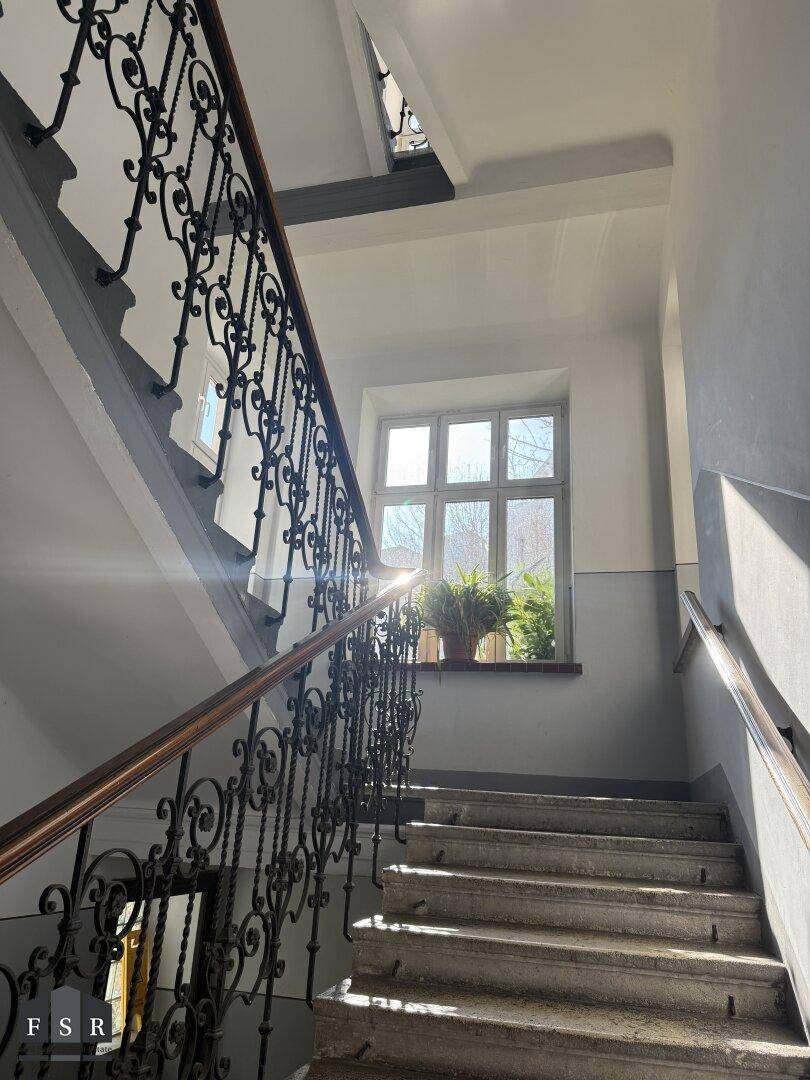 Detailansicht des Treppenhauses mit schmiedeeisernem Geländer und einem Fenster, das die Treppe erhellt und schmückt.
