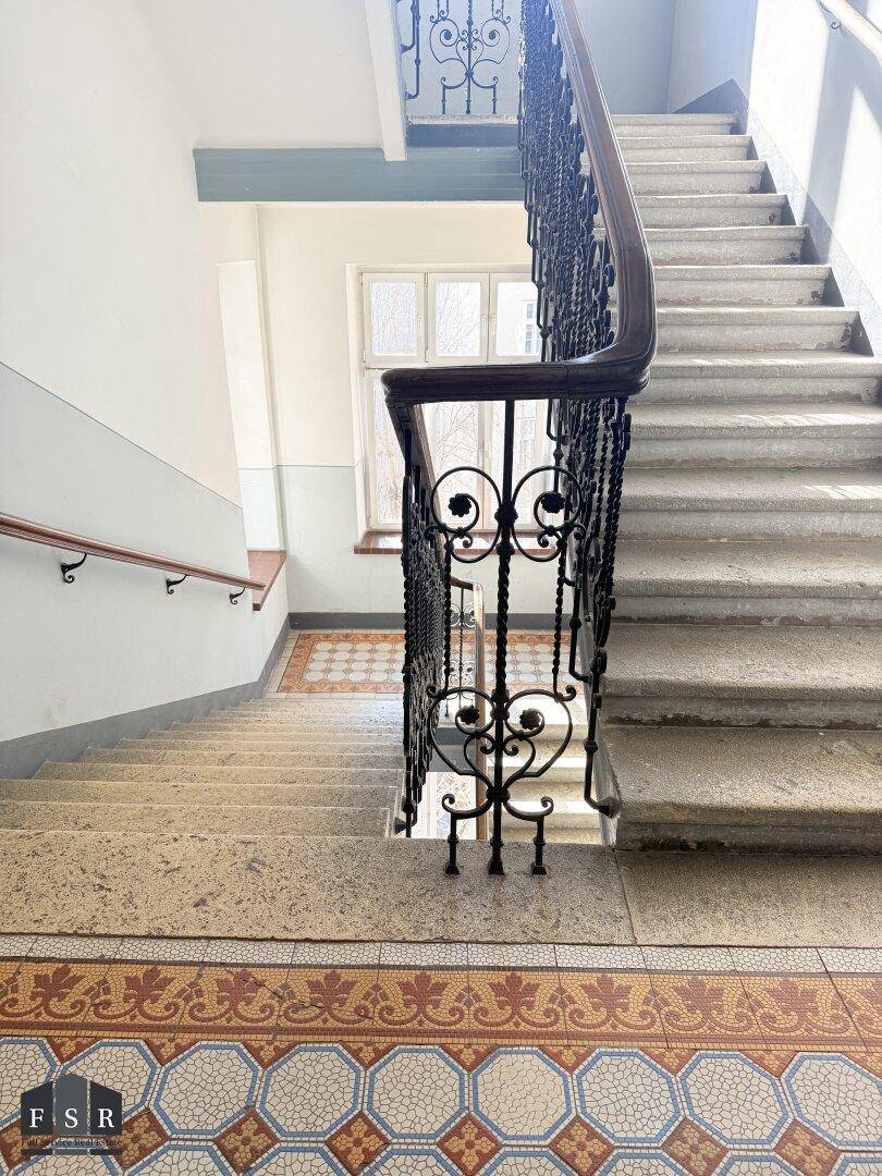 Treppenhaus mit kunstvollen Fliesenmustern und einem eleganten schmiedeeisernen Geländer, das den historischen Charme bewahrt.