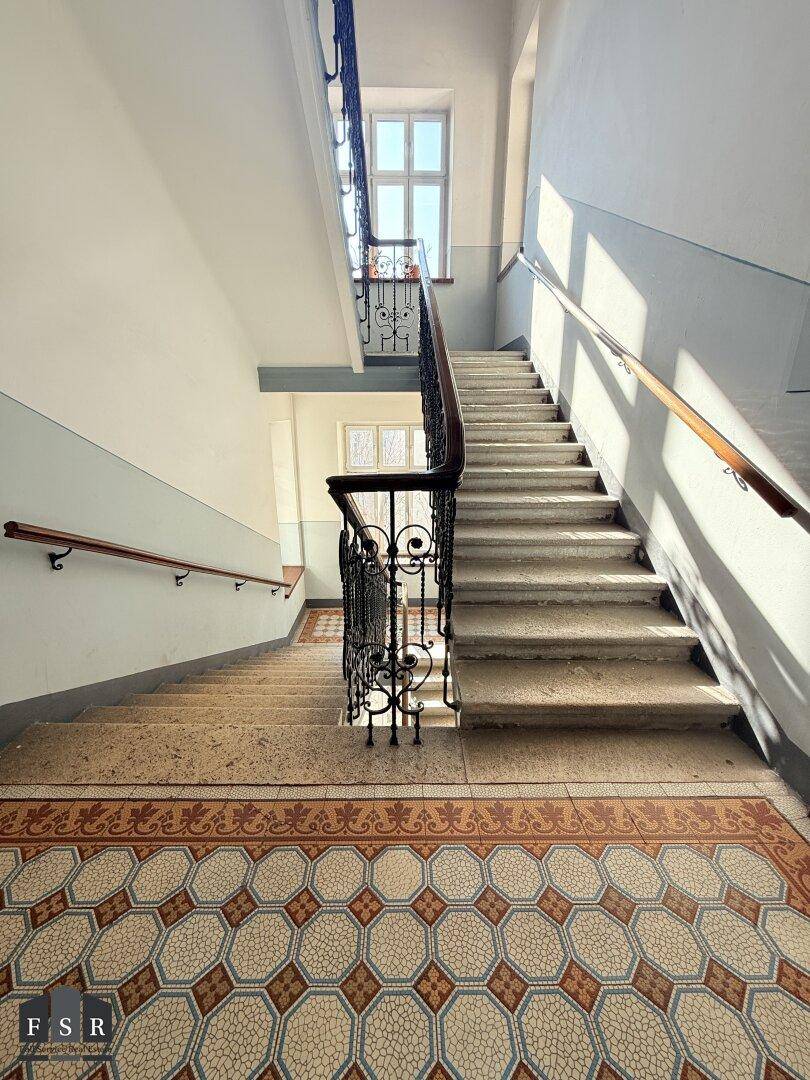 Historisches Treppenhaus mit kunstvollem Geländer, Steinstufen und gemusterten Fliesen.
