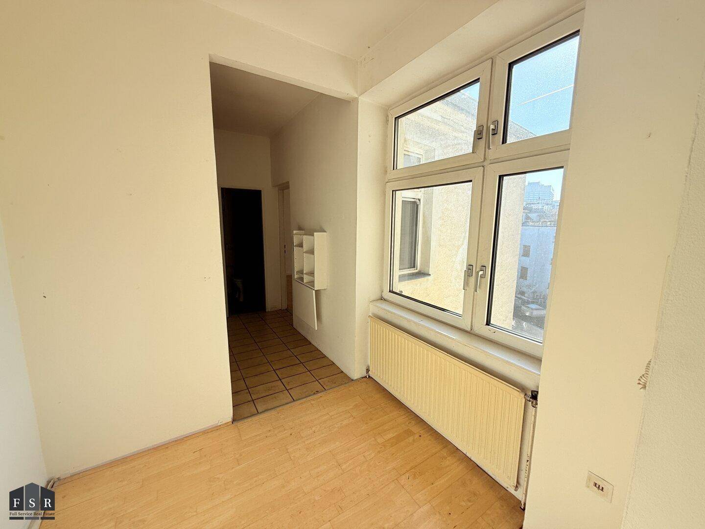 Lichtdurchfluteter Bereich mit Parkettboden und großem Fenster, das viel Tageslicht hereinlässt.