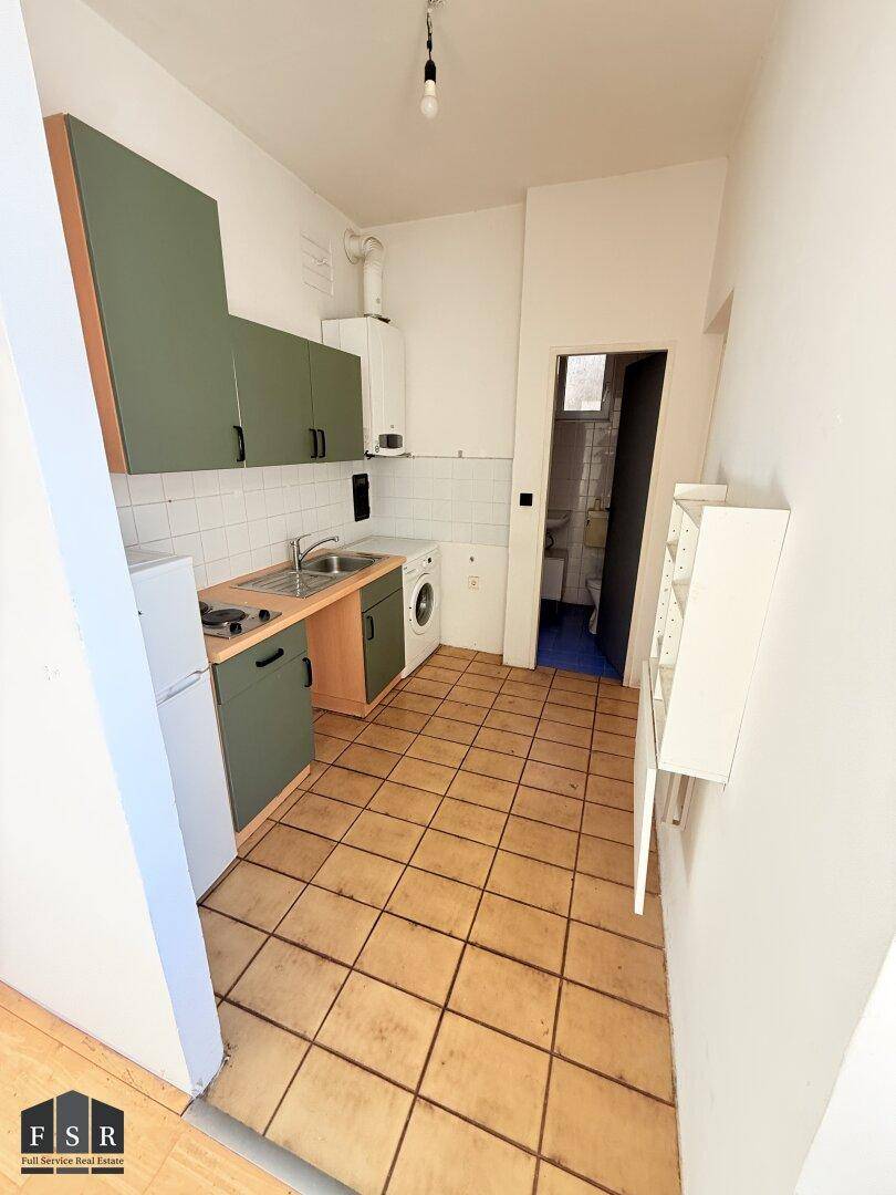 Kleine Küche mit grünen Schränken, Spüle, Kühlschrank und Waschmaschine, mit Zugang zum Bad.