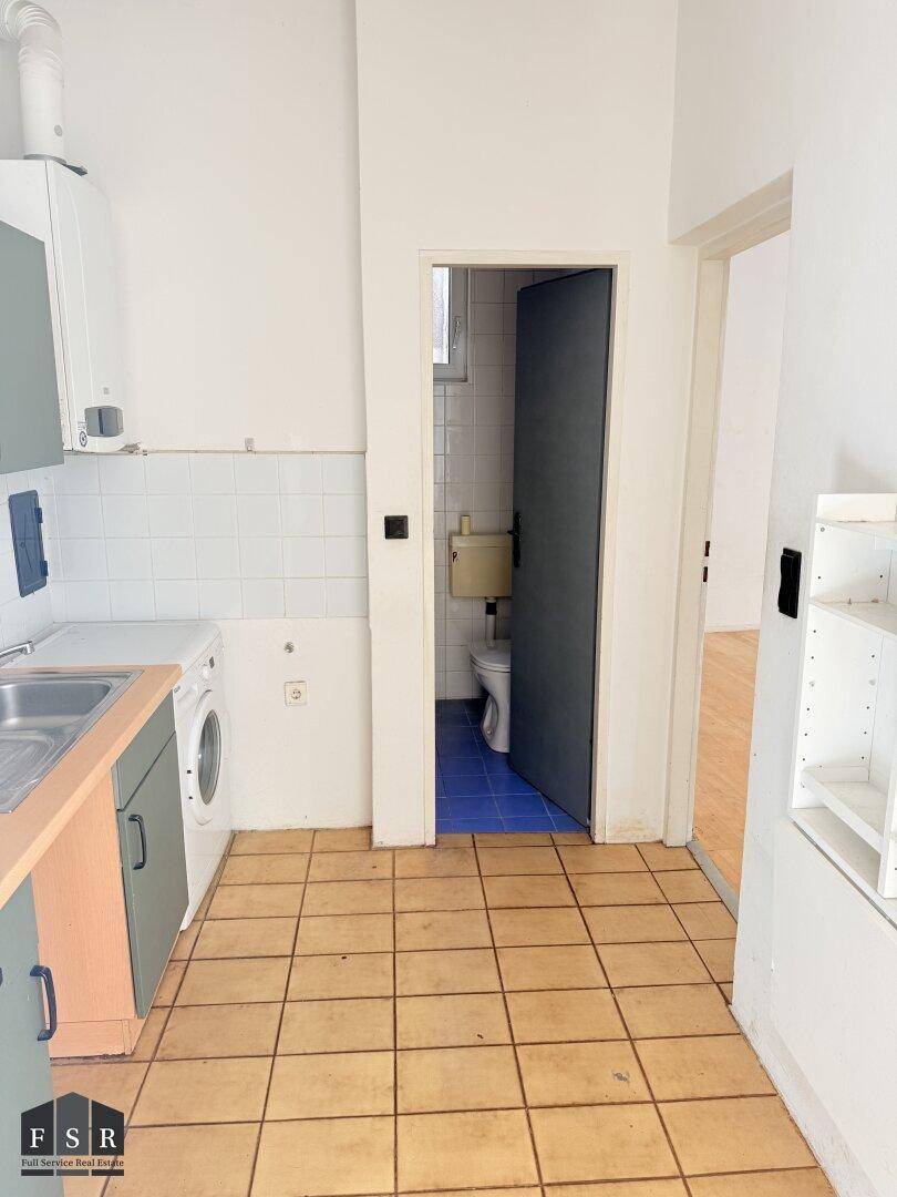 Kompakte Küche mit Fliesenboden und Blick auf das angrenzende Badezimmer.