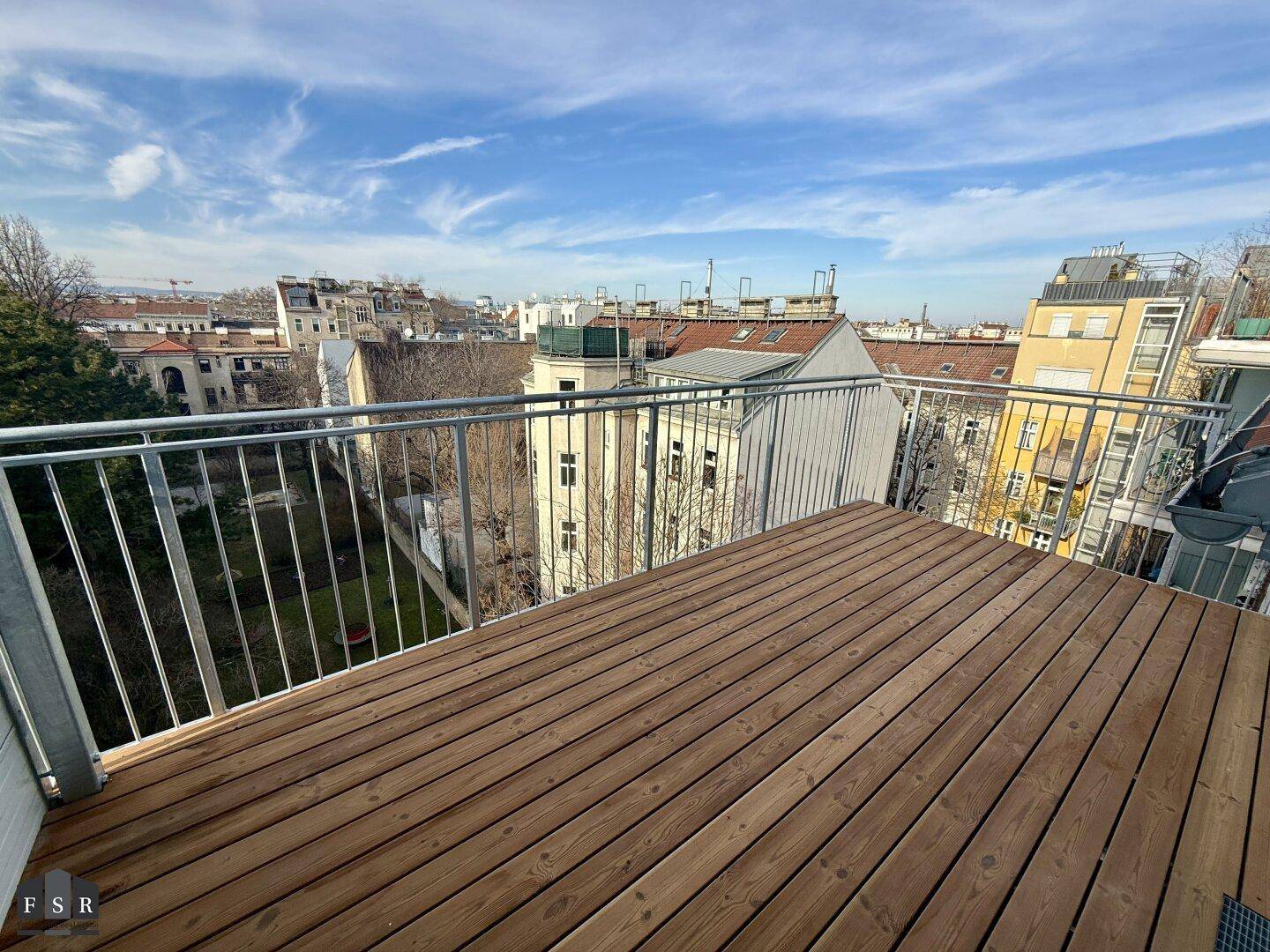 Sonniger Balkon mit Holzdielen und weitem Blick über die Stadt.