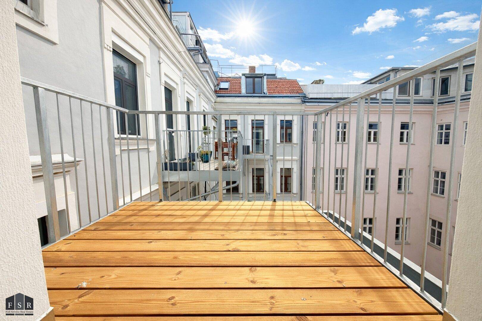 Sonniger Balkon mit Holzboden und Metallgeländer, bietet einen Blick auf den Innenhof.