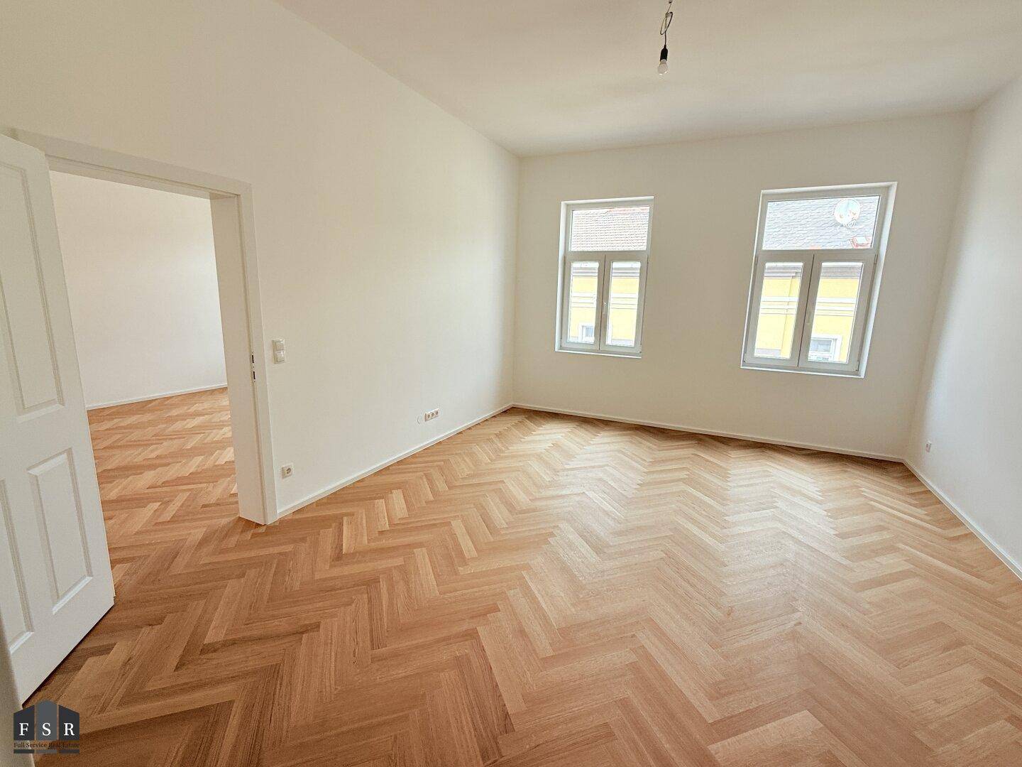 Geräumiges Zimmer mit hellem Fischgrätparkett, hohen Decken und großen Fenstern.
