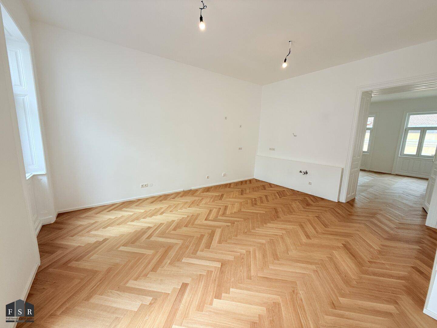 Geräumiges Zimmer mit Fischgrätparkett, hohen Decken und vorbereiteten Anschlüssen an der Wand.
