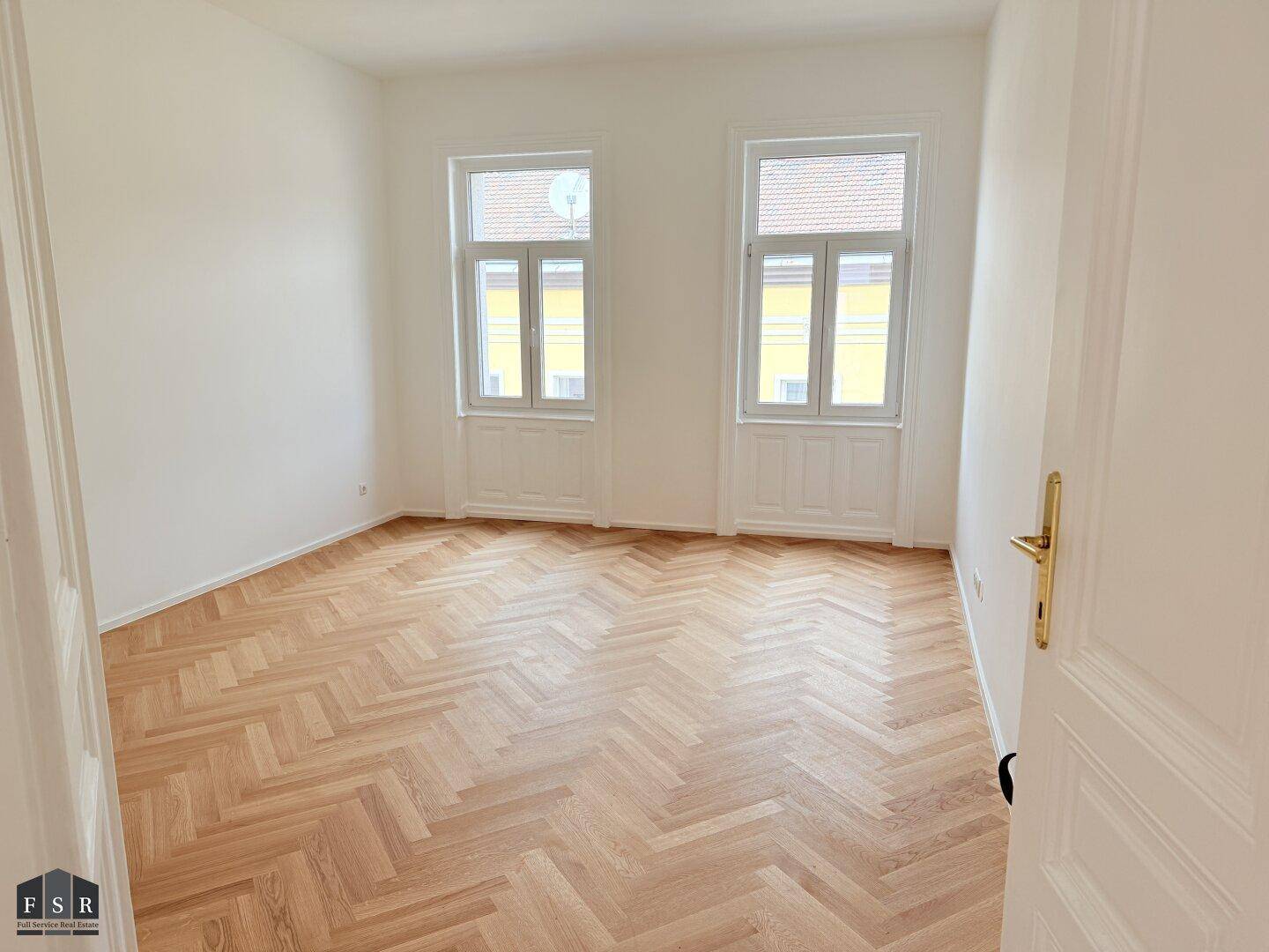 Helles Schlafzimmer mit klassischem Fischgrätparkett, hohen Decken und zwei großen Fenstern.