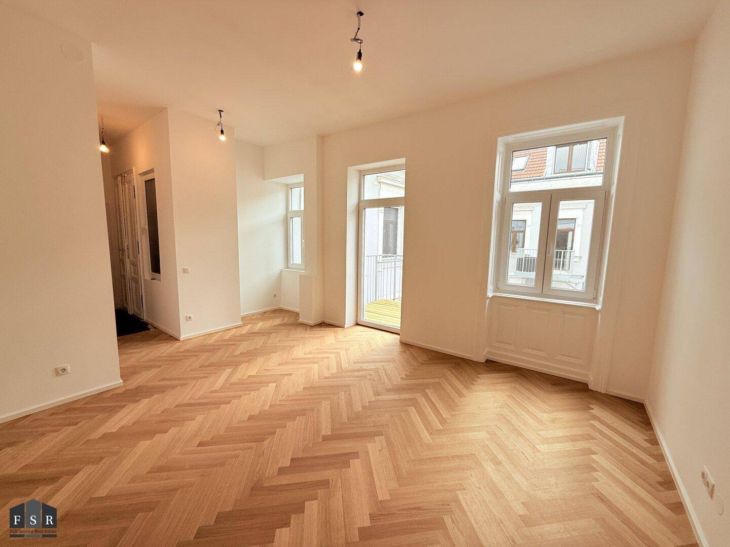 Großes Wohnzimmer mit Fischgrätparkett, hohen Decken und direktem Zugang zum Balkon.