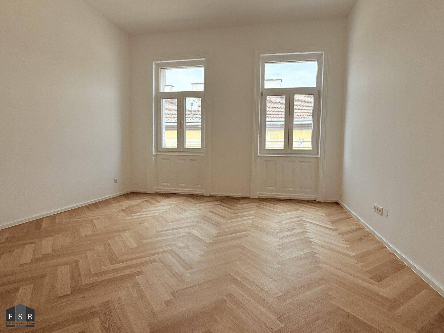 Helles Schlafzimmer mit Fischgrätparkett, hohen Decken und zwei großen Fenstern zur Straße.