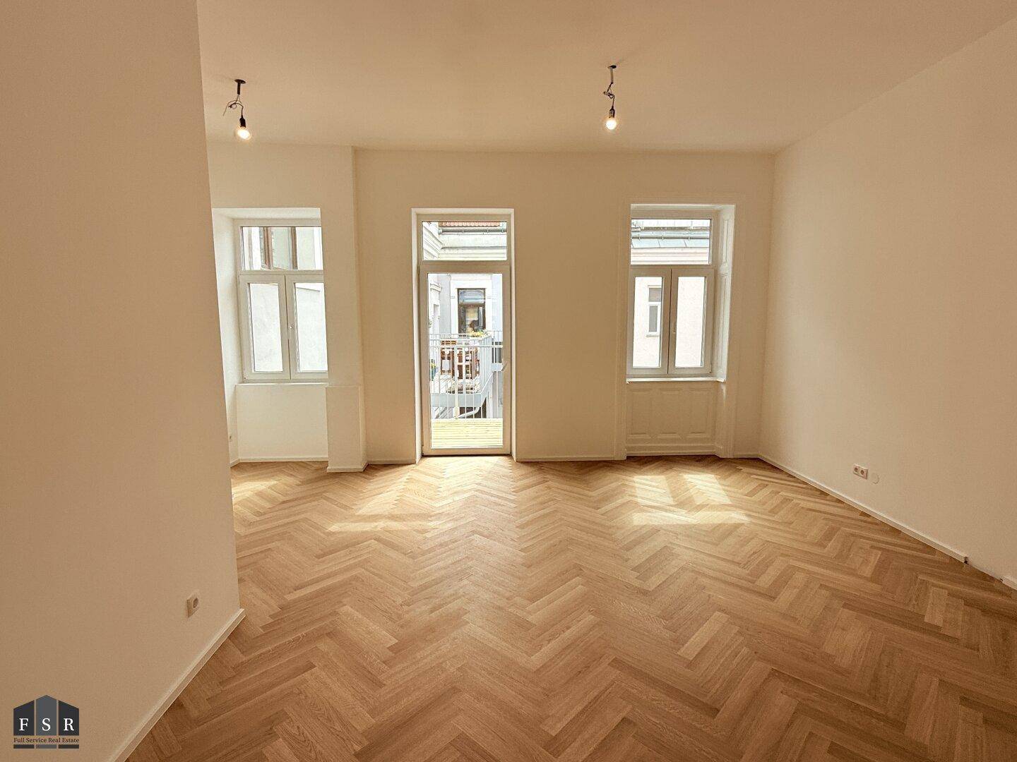 Großes Wohnzimmer mit Fischgrätparkett, hohen Decken und direktem Zugang zum Balkon.
