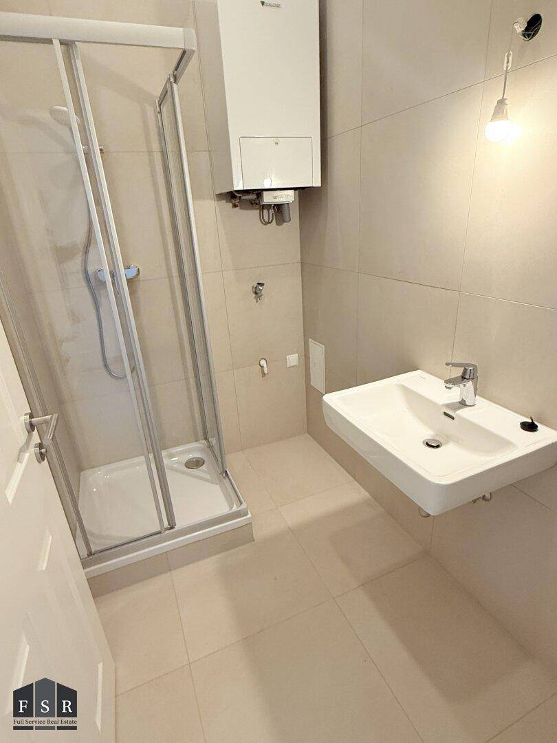 Modernes Badezimmer mit Duschkabine, Waschbecken und Warmwasserbereiter an der Wand.
