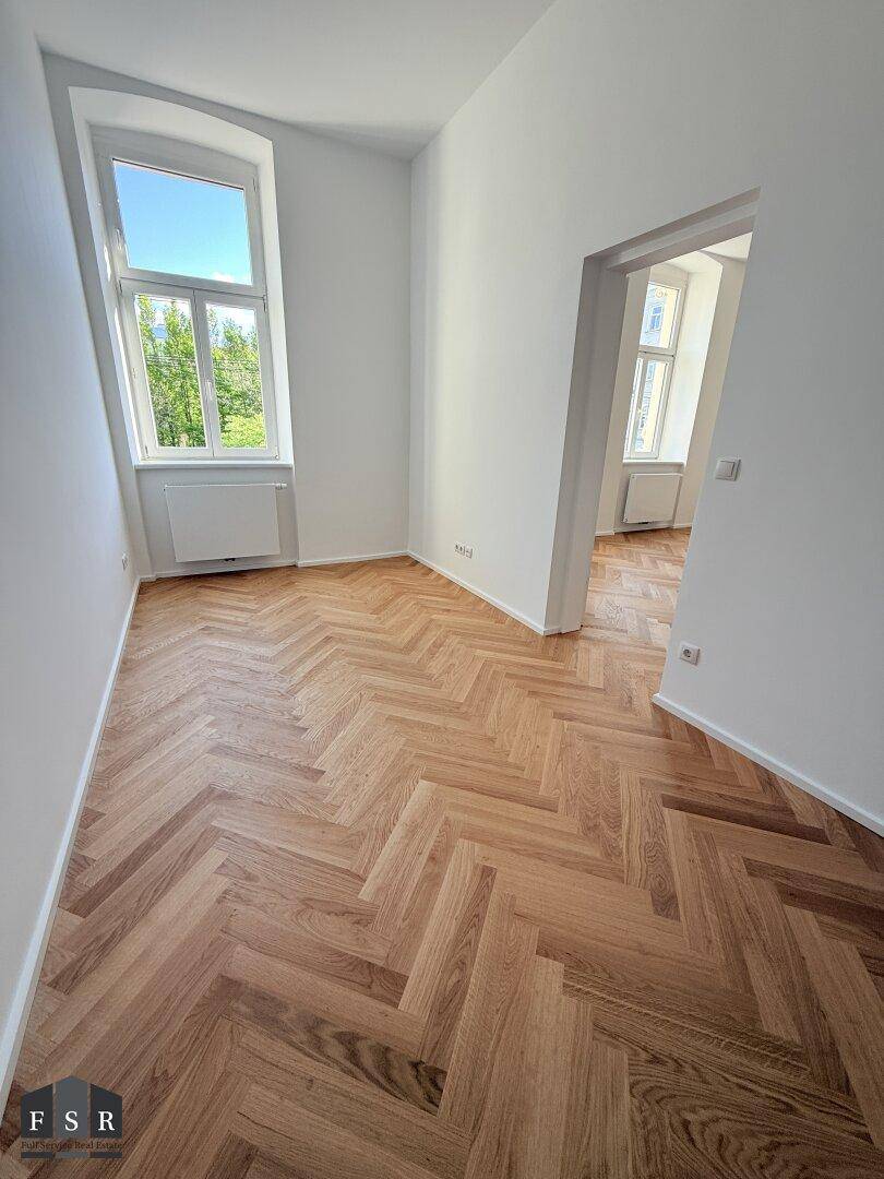 Helles Zimmer mit Fischgrätparkett und einem Fenster mit Blick ins Grüne.