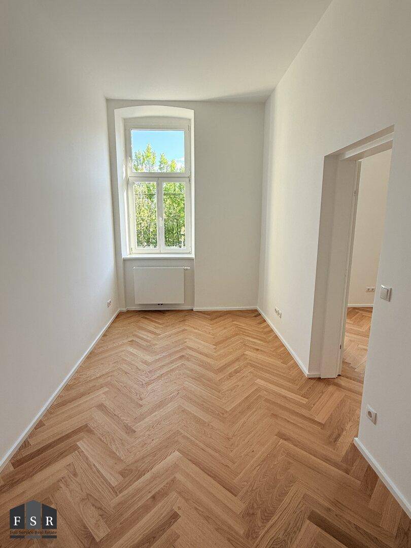 Helles Zimmer mit Fischgrätparkett und einem Fenster, ideal als Schlaf- oder Arbeitszimmer.