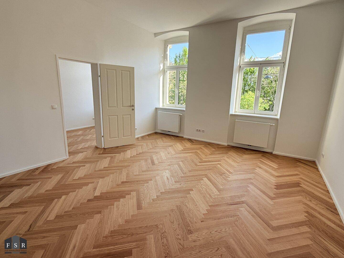 Helles Wohnzimmer mit neu verlegtem Fischgrätparkett und zwei großen Fenstern mit Blick ins Grüne.