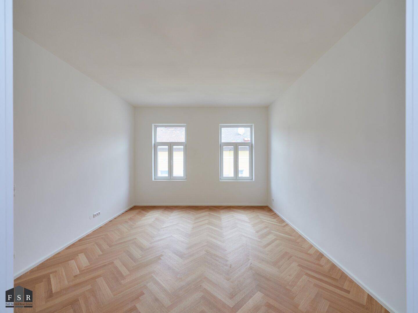 Helles, leeres Zimmer mit Fischgrätparkettboden und zwei Fenstern, bereit zur individuellen Gestaltung.