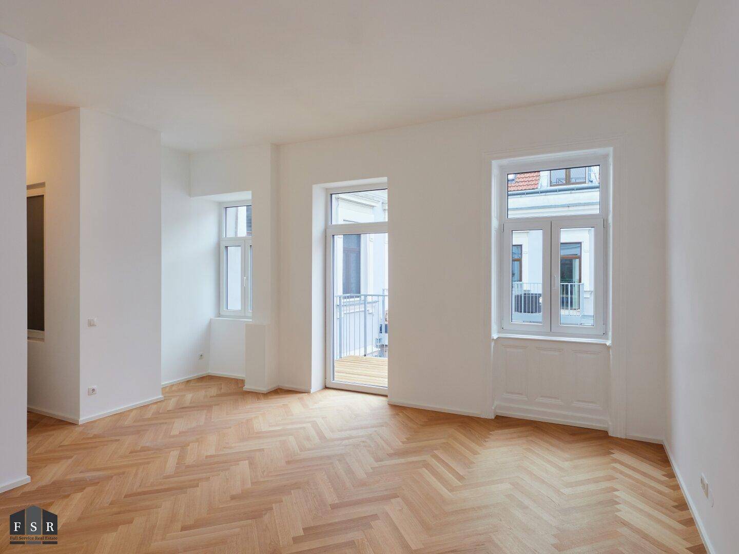 Geräumiger, heller Raum mit Fischgrätparkett und direktem Zugang zu einem kleinen Balkon.
