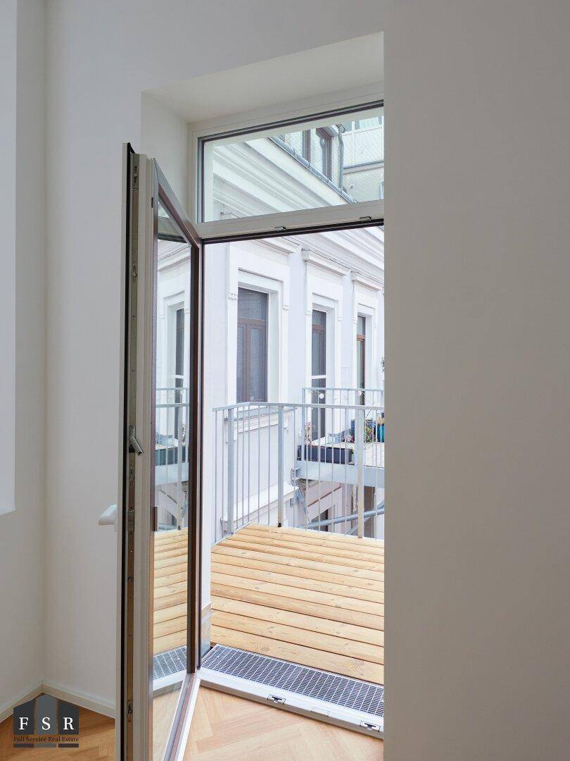 Offene Balkontür mit Blick auf den Holzbalkon und die umliegenden Gebäude im Innenhof.