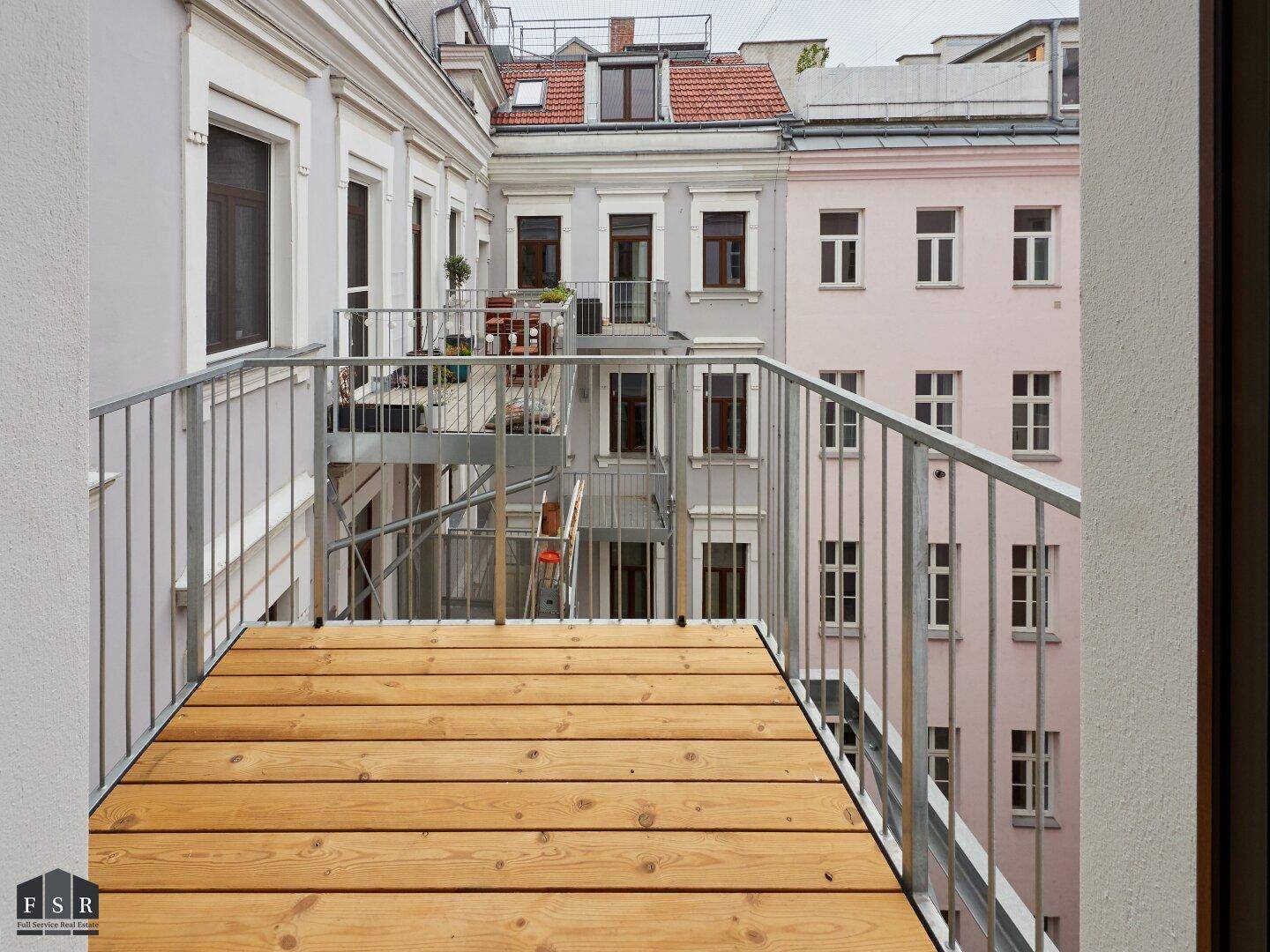 Kleiner Holzbalkon mit Metallgeländer und Blick auf die Innenhofbebauung.