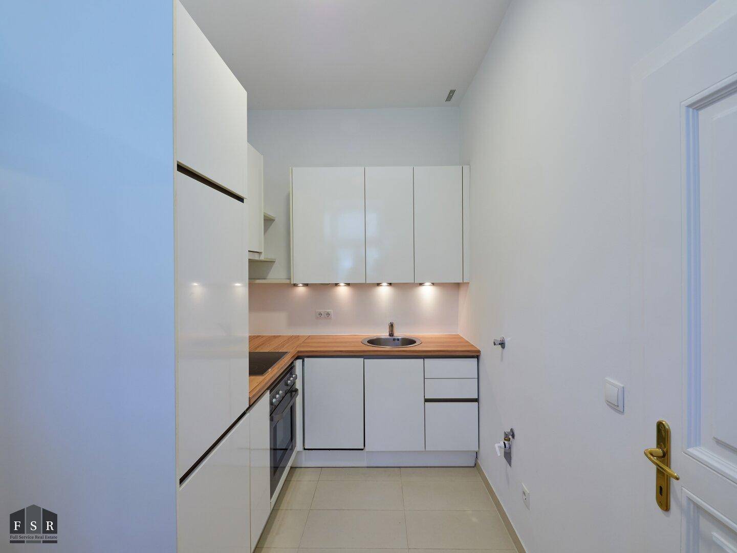 Kompakte Einbauküche mit hellen Fronten, Holzdetails und modernen Kochgeräten, ideal für kleine Räume.