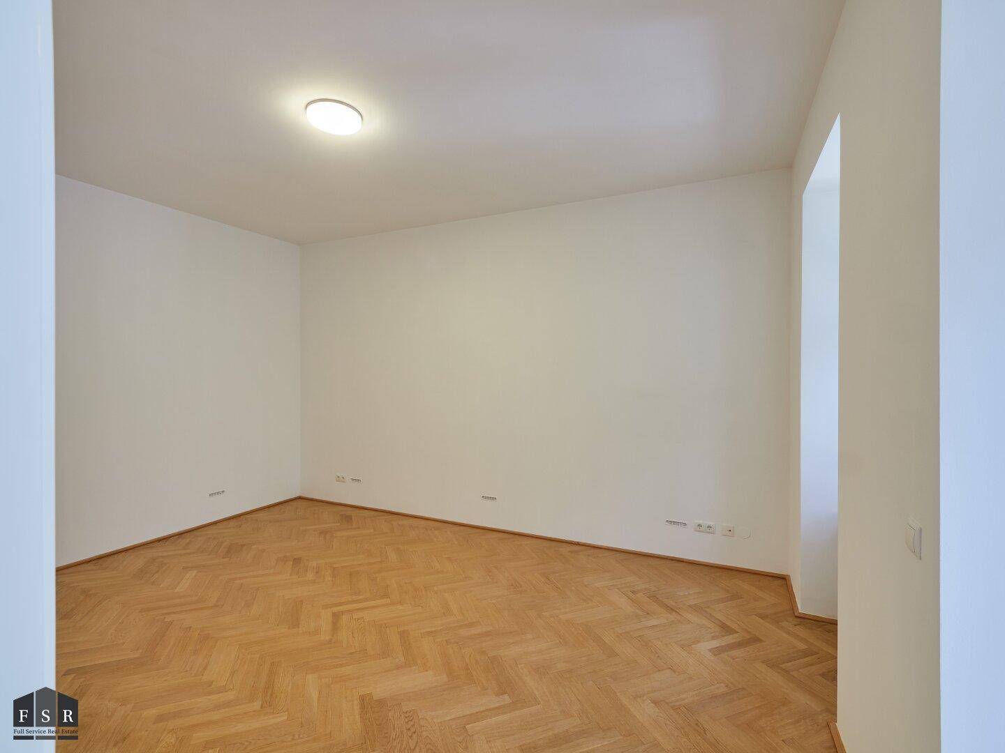 Leeres Zimmer mit Fischgrätparkett und weiß gestrichenen Wänden, bereit zur individuellen Gestaltung.