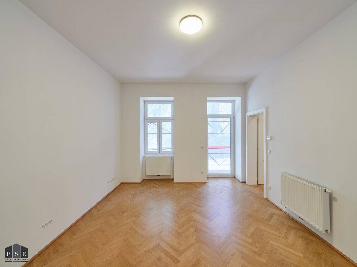 Helles Zimmer mit Parkettboden, großen Fenstern und Heizkörper, ideal für Wohn- oder Schlafbereich.