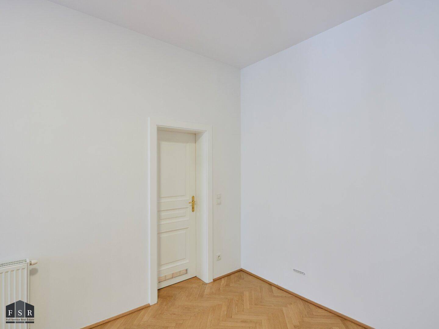 Leeres Zimmer mit Parkettboden und weißer Tür, bietet vielseitige Nutzungsmöglichkeiten für Bewohner.