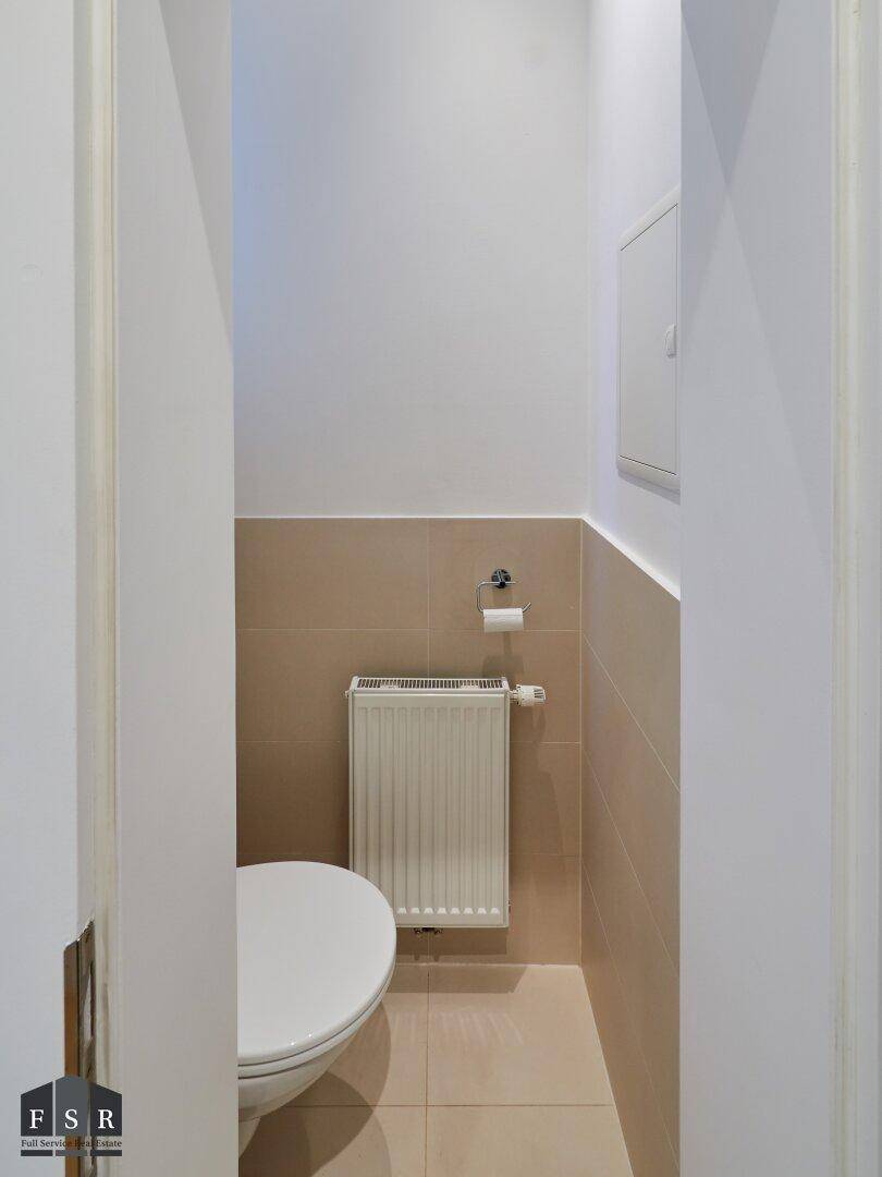 Kleines Gäste-WC mit Wand-WC, Heizkörper und beigefarbenen Fliesen an den Wänden.