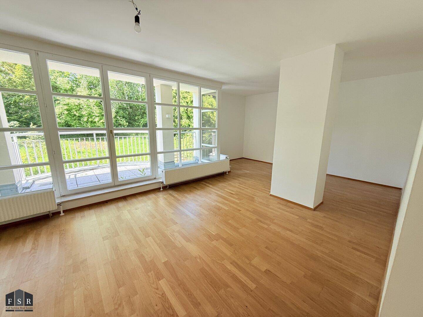 Großzügiges Wohnzimmer mit Parkettboden und breiter Fensterfront zum Außenbereich.
