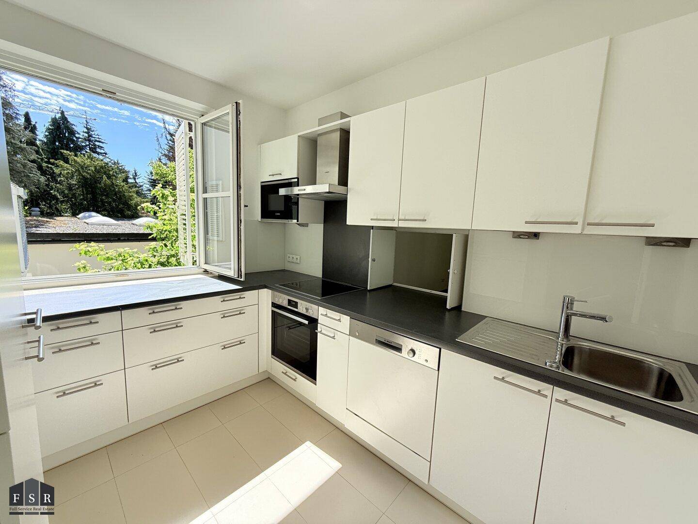 Moderne Einbauküche mit weißen Hochglanzfronten, dunkler Arbeitsplatte und Fenster.