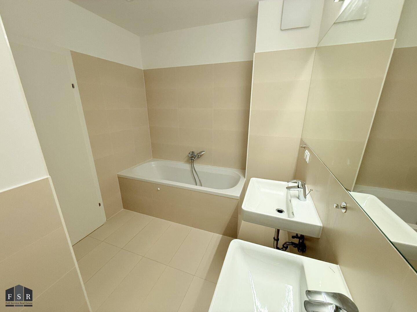 Badezimmer mit Badewanne, Doppelwaschbecken und großem Spiegel, hell gefliest.