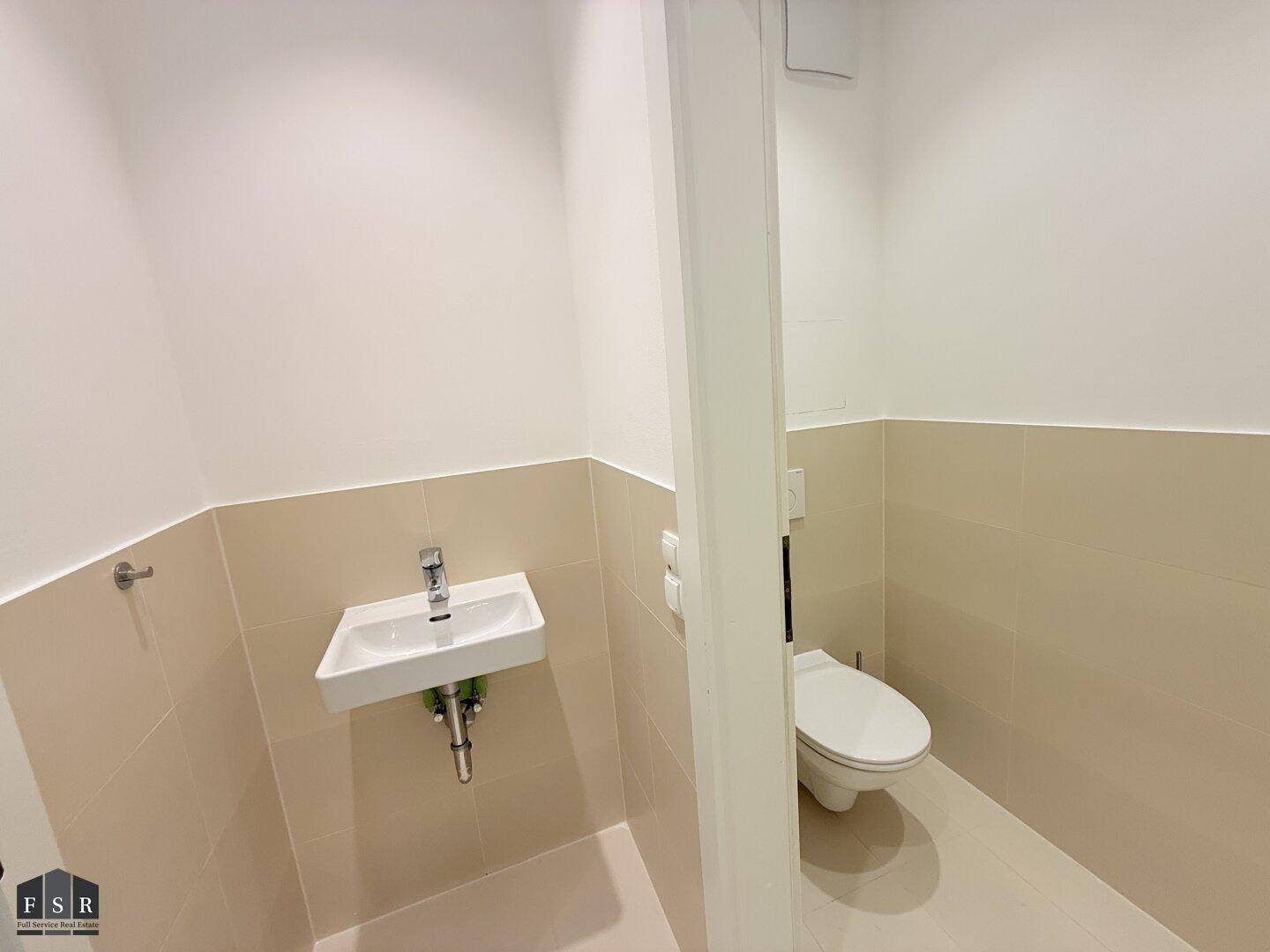 Separate Gästetoilette mit Wand-WC, kleinem Waschbecken und hellen Fliesen.