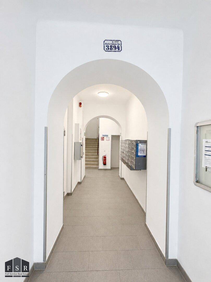 Heller Eingangsbereich mit gewölbten Durchgängen, Fliesenboden und Briefkästen.