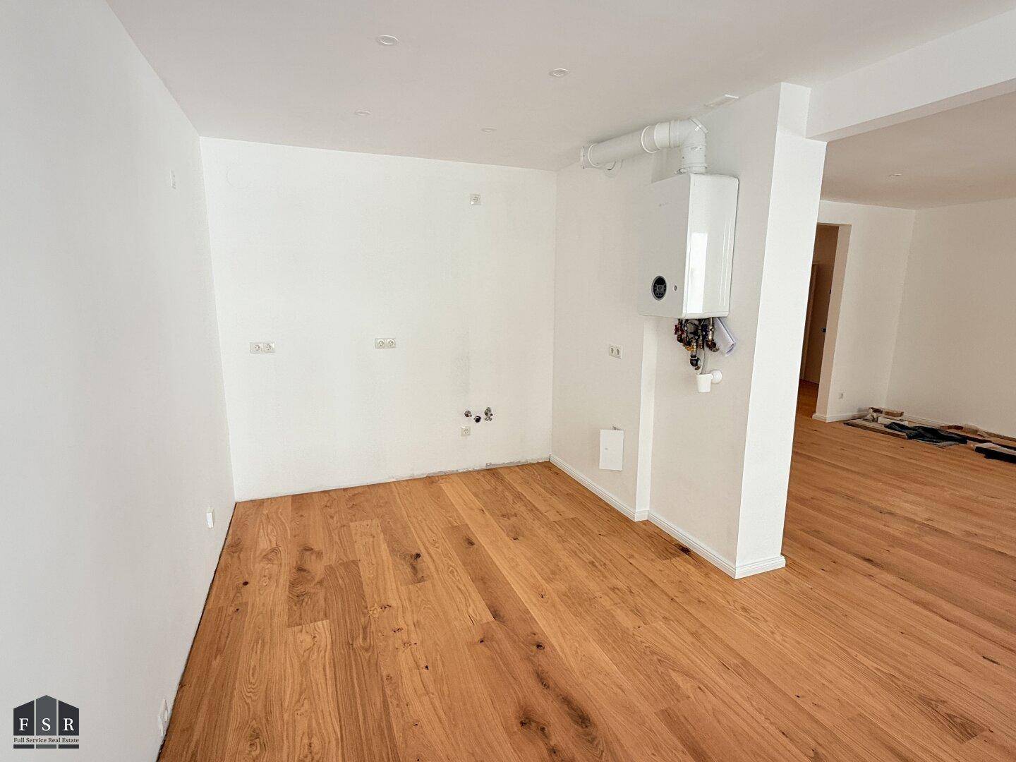 Leerer Küchenbereich mit Anschlüssen für Geräte und Heiztherme, bereit für Einbauküche.