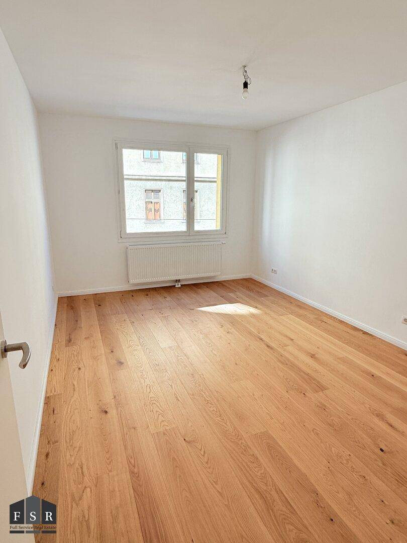 Helles Schlafzimmer mit Parkettboden und einem großen Fenster, das viel Licht hereinlässt.