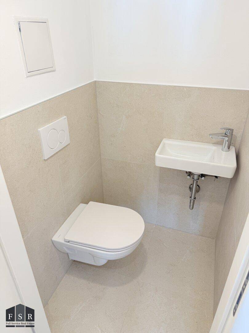 Kleines, modernes Gäste-WC mit Wand-WC, Handwaschbecken und hellen Fliesen.