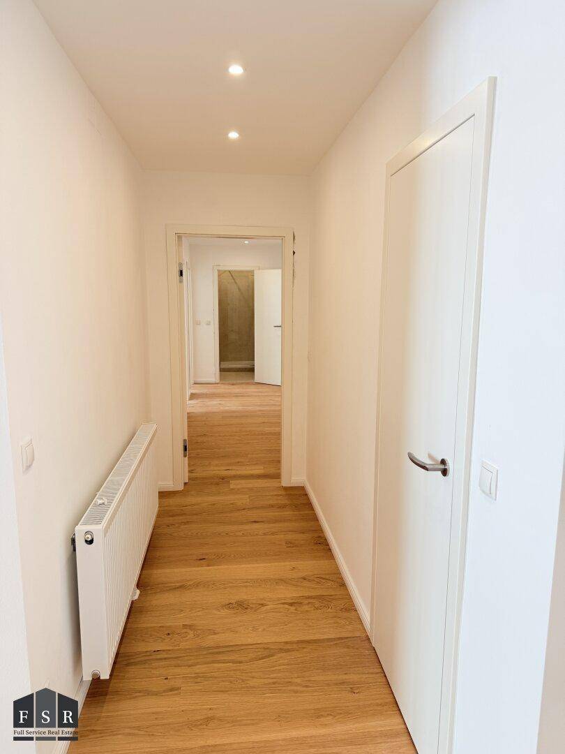 Langer, heller Flur mit Holzfußboden und Einbaustrahlern in der Decke.