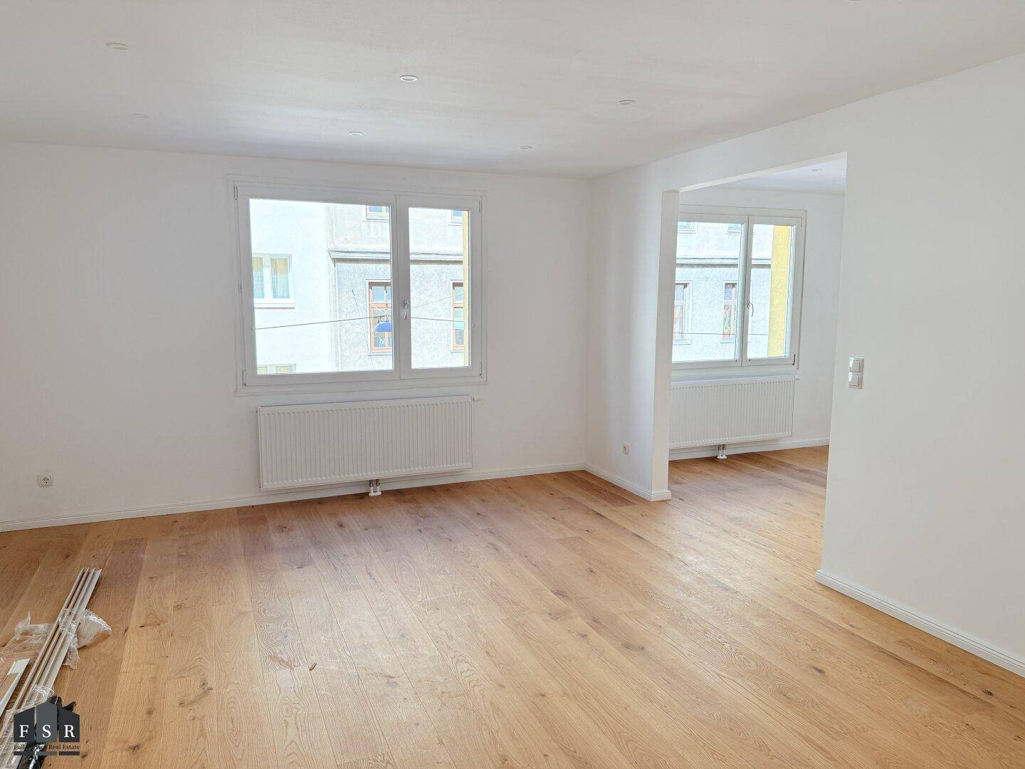 Lichtdurchfluteter Wohnbereich mit großen Fenstern und neu verlegtem Holzparkett.