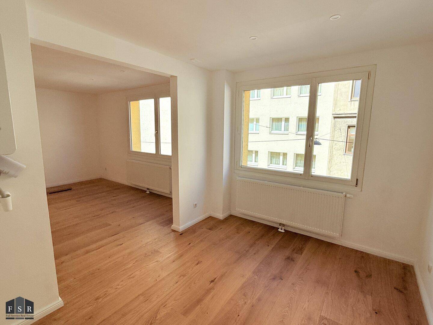 Heller Wohnraum mit Blick auf die umliegenden Gebäude und hochwertigem Parkettboden.
