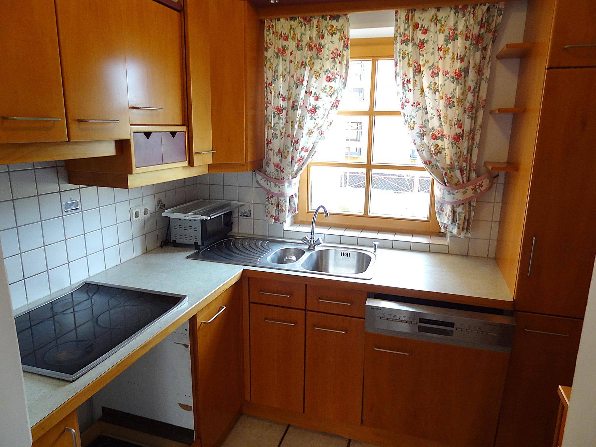 Gemütliche Küche mit Holzschränken, Spüle am Fenster und integriertem Geschirrspüler.