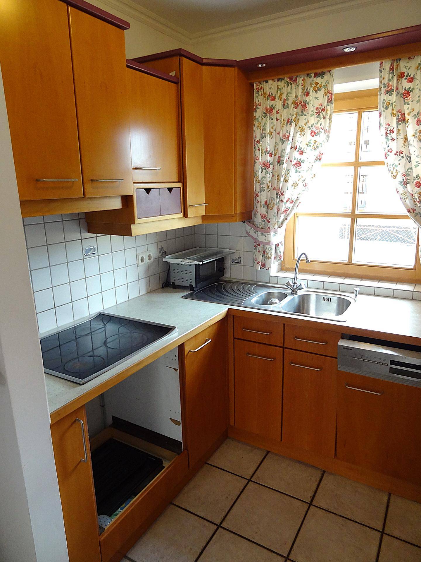 Funktionale Küche mit hellen Holzfronten, Fliesenrückwand und Blick auf das Fenster.