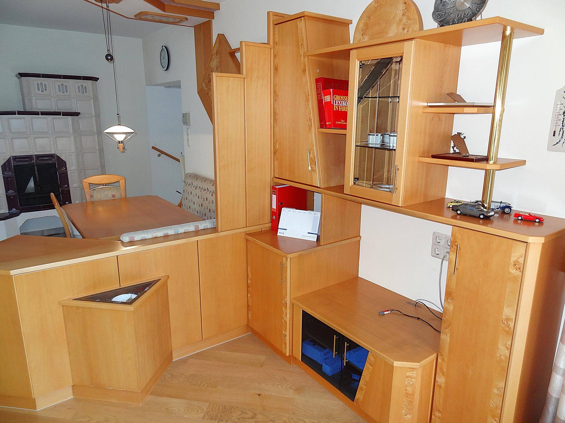 Wohnbereich mit Holzmöbeln, Stauraum und Blick auf den traditionellen Kachelofen.