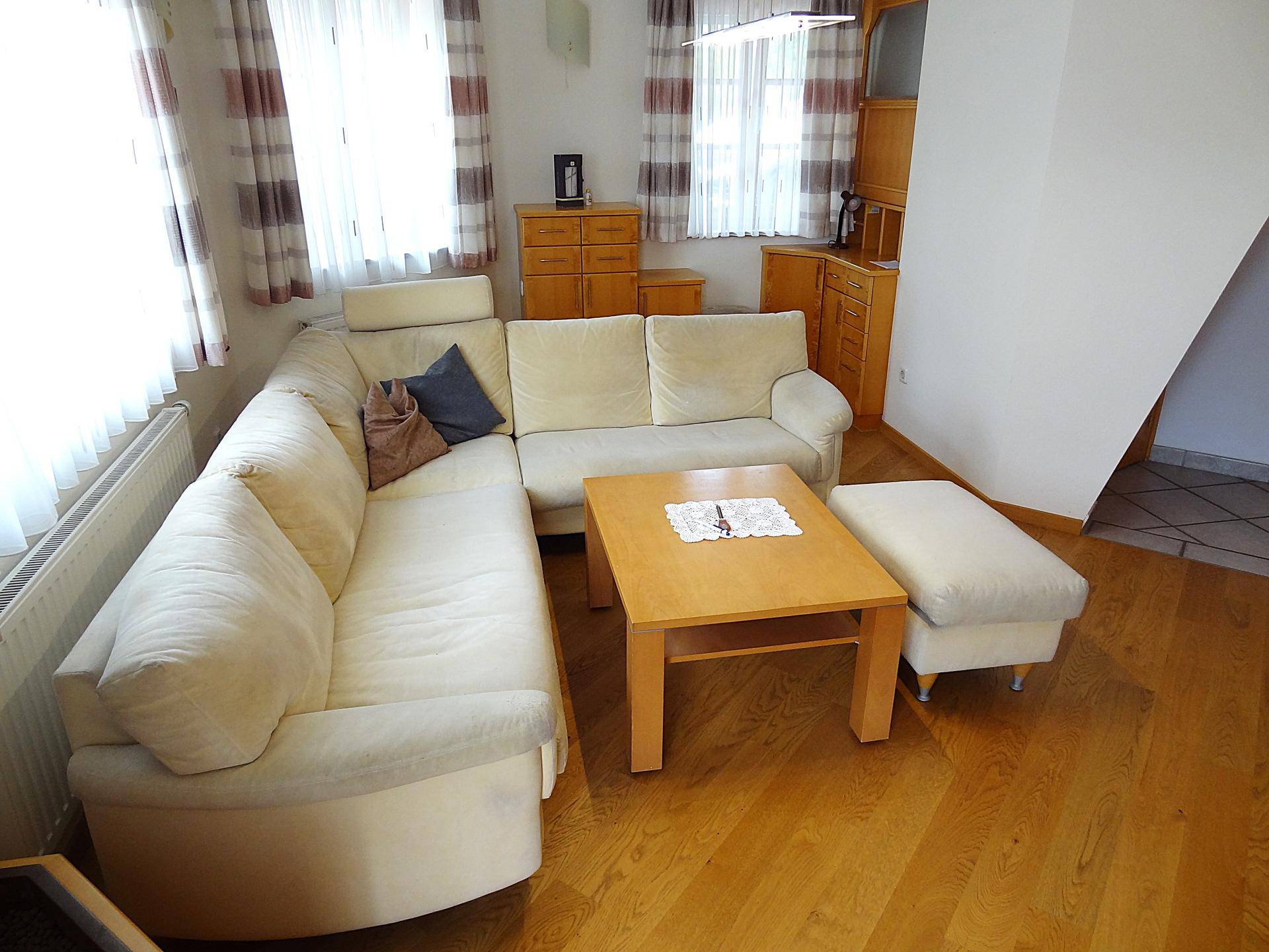 Komfortables Wohnzimmer mit großem Ecksofa, Holztisch und viel Tageslicht.