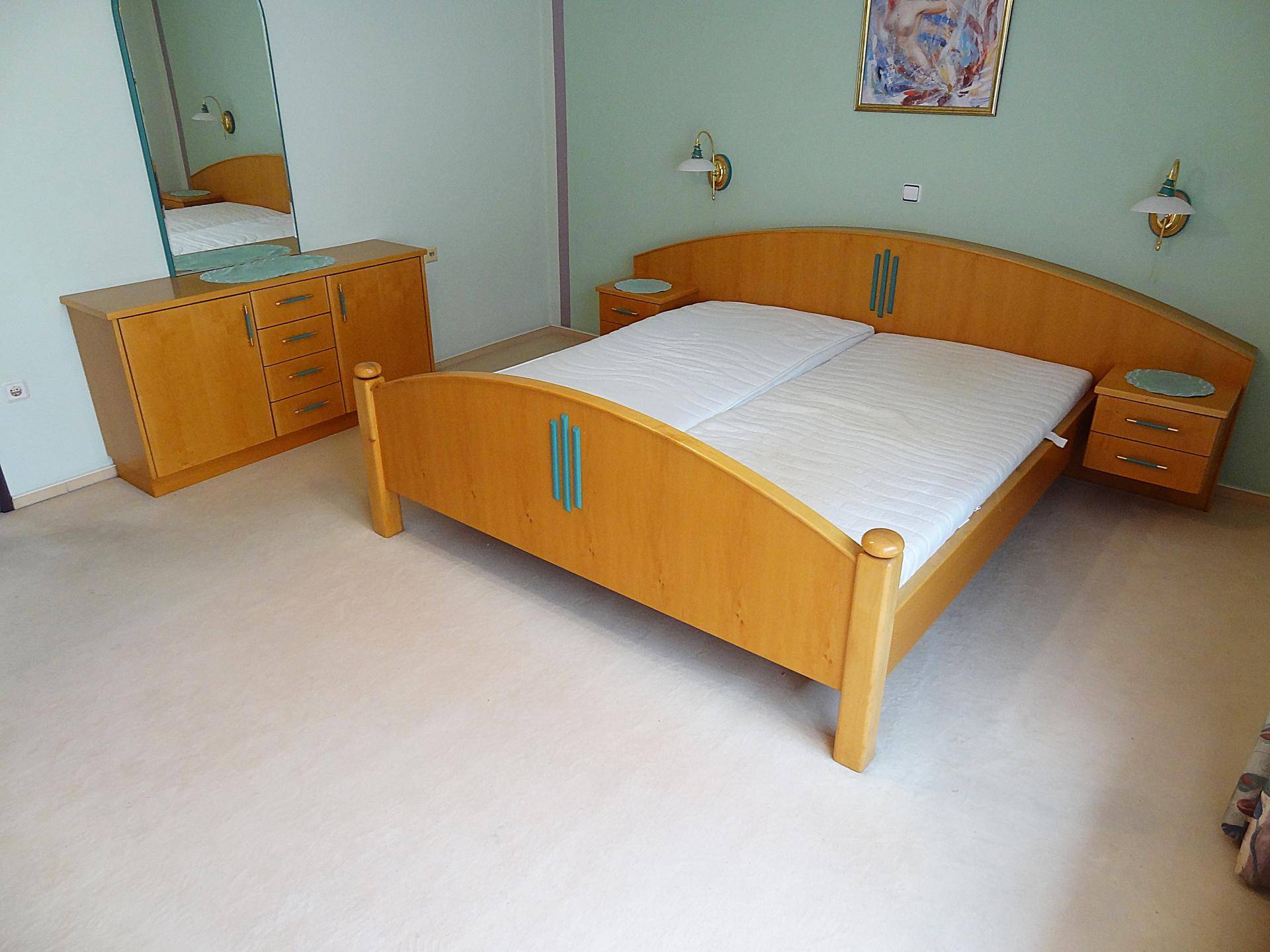 Schlafzimmer mit Holzdoppelbett, Kommode und Spiegel, in hellem Ambiente.