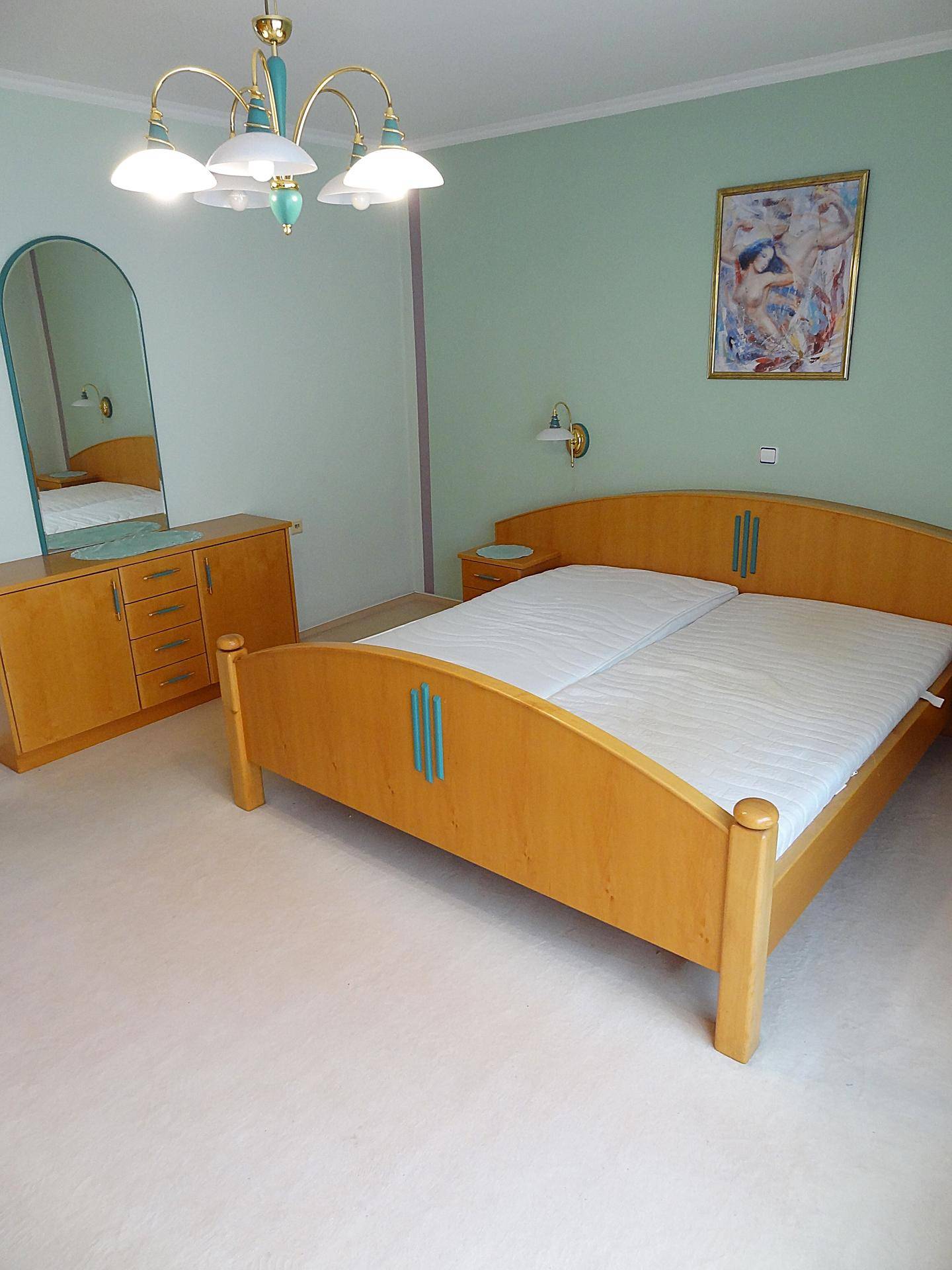 Helles Schlafzimmer mit Doppelbett, Kommode und Spiegel, in freundlicher Atmosphäre.