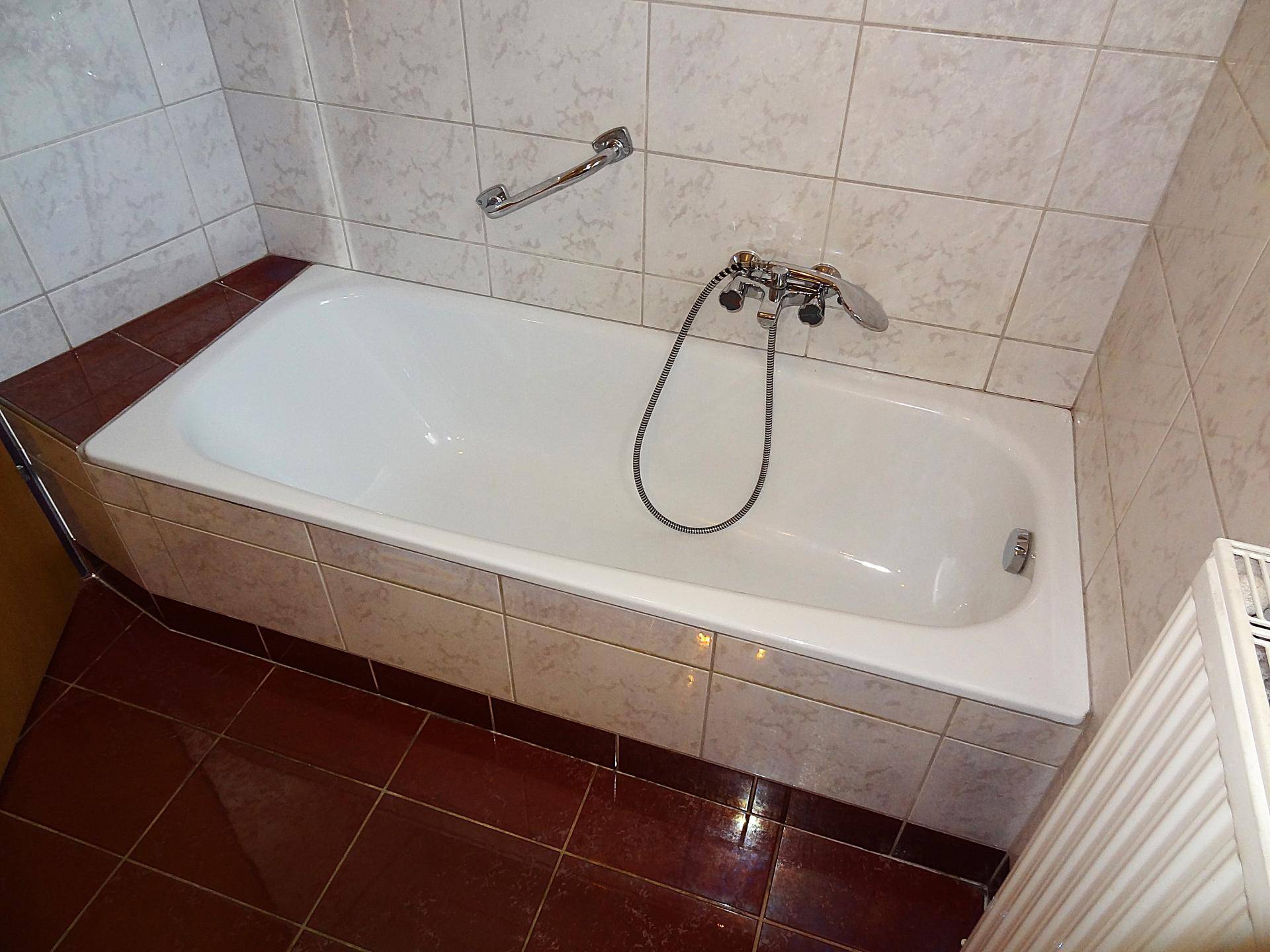 Eingebaute Badewanne mit Fliesenverkleidung und Handlauf, in einem gefliesten Badezimmer.