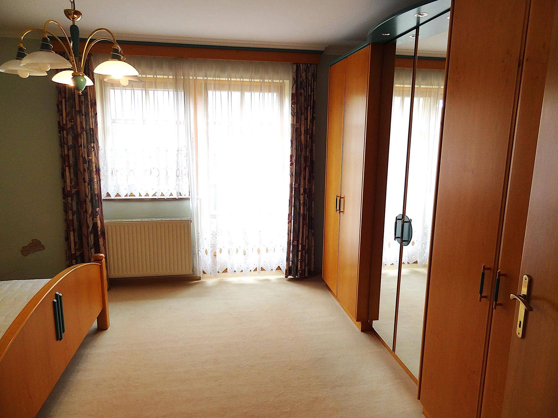 Schlafzimmer mit großem Spiegelschrank, Doppelbett und Fenster mit Vorhängen.